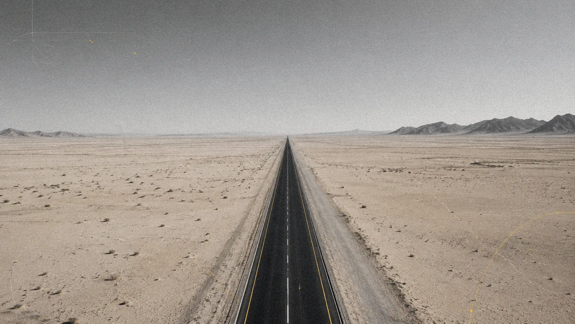 Straight desert road running toward distant mountains under a pale skyscraped sky