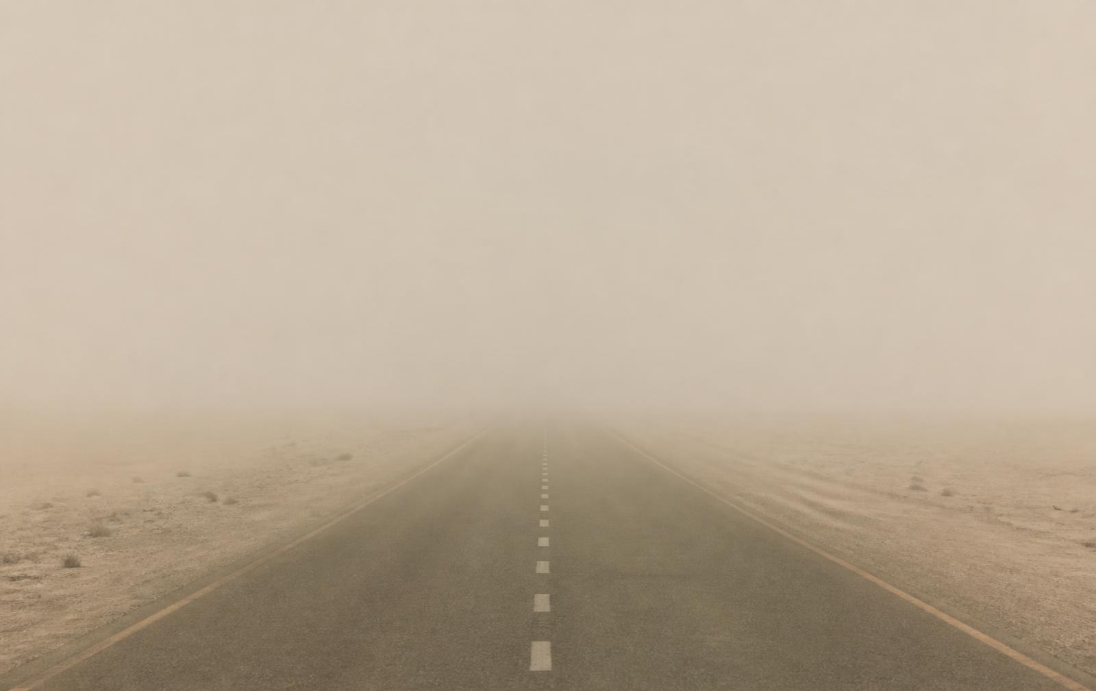 Open desert road running towards the horizon in pale haze